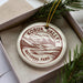 A circular ornament with the text "KOBUK VALLEY NATIONAL PARK USA" printed on it, placed inside a box with pine branches.