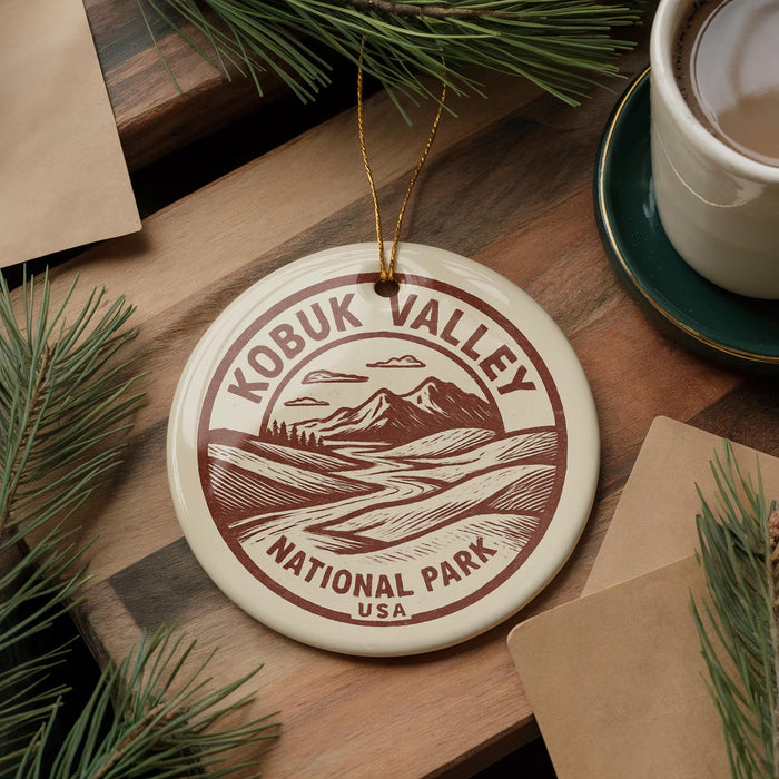 A circular ornament with the text "KOBUK VALLEY NATIONAL PARK USA" printed on it, surrounded by pine branches and a cup of coffee on a wooden surface.