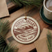 A circular ornament with the text "KOBUK VALLEY NATIONAL PARK USA" printed on it, surrounded by pine branches and a cup of coffee on a wooden surface.