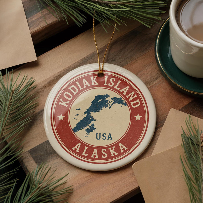 A circular ornament with the text "KODIAK ISLAND USA" and a map of Alaska, surrounded by pine branches and a cup of coffee on a wooden surface.