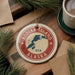 A circular ornament with the text "KODIAK ISLAND USA" and a map of Alaska, surrounded by pine branches and a cup of coffee on a wooden surface.