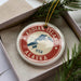 A circular ornament with the text "KODIAK ISLAND" and "USA" printed on it, surrounded by pine branches.