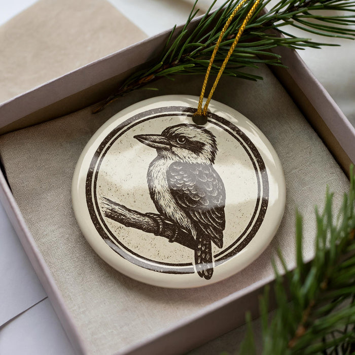 A ceramic ornament in the shape of a bird, specifically a kookaburra, is displayed in a box with pine branches.