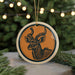A ceramic ornament featuring a detailed illustration of a deer or antelope with large curved horns, hanging on a string and surrounded by pine branches.