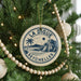 A Christmas tree decorated with ornaments, including a circular ornament with a palm tree and a beach scene, and a beaded ornament.