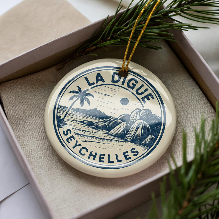 A circular ornament with a palm tree and mountains, featuring the text "LA DIGUE SEYCHELLES" on it, is displayed in a box with pine branches.