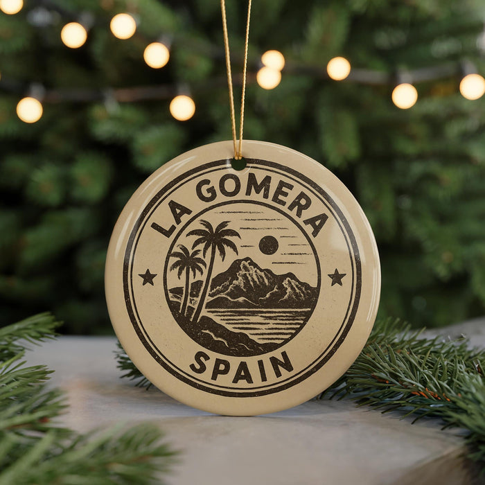 A circular ornament with the text "LA GOMERA SPAIN" printed on it, featuring a palm tree and mountain landscape design.