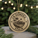 A circular ornament with the text "LA GOMERA SPAIN" printed on it, featuring a palm tree and mountain landscape design.