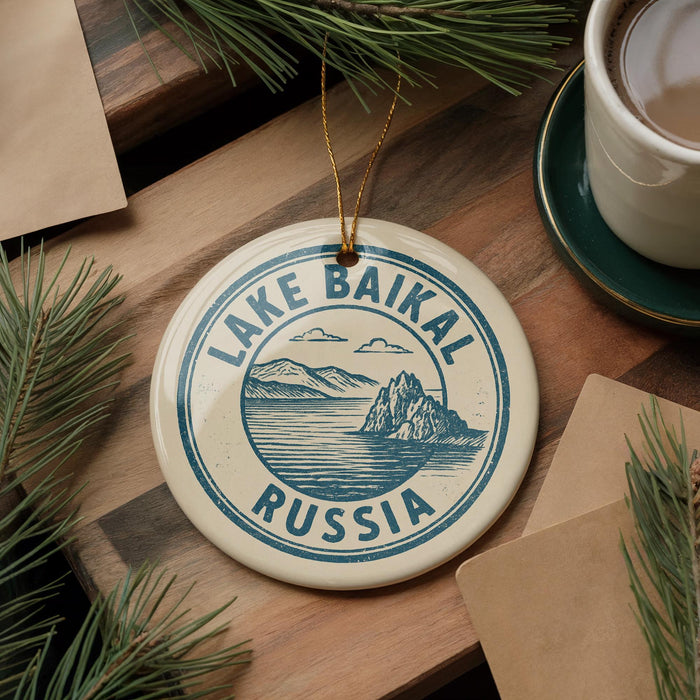 A circular ornament with the text "LAKE BAIKAL RUSSIA" printed on it, surrounded by pine branches and a cup of coffee on a wooden surface.