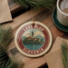 A circular ornament with the text "LAKELI BLED SLOVENIA" and an illustration of a lake and a church, hanging on a wooden surface.