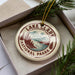 A circular ornament with the text "LAKELAND NATIONAL PARK USA" printed on it, surrounded by pine branches.