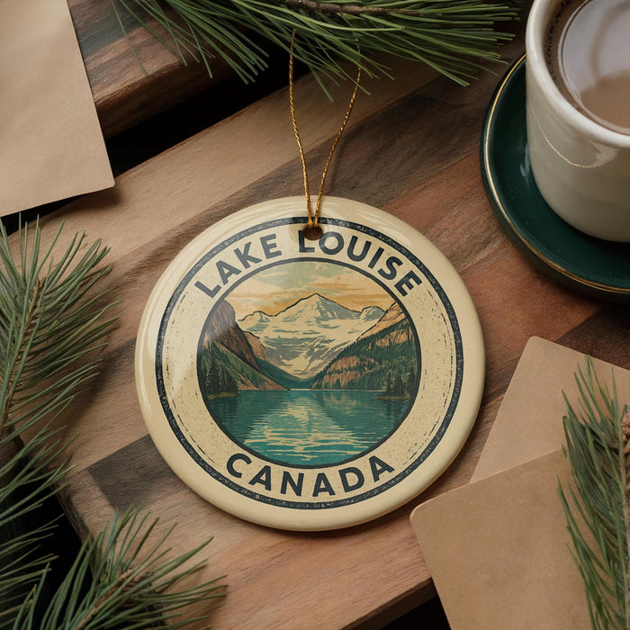 A circular ornament with the text "LAKELIKE CANADA" and a mountain landscape design, placed on a wooden surface next to a cup of coffee and pine branches.