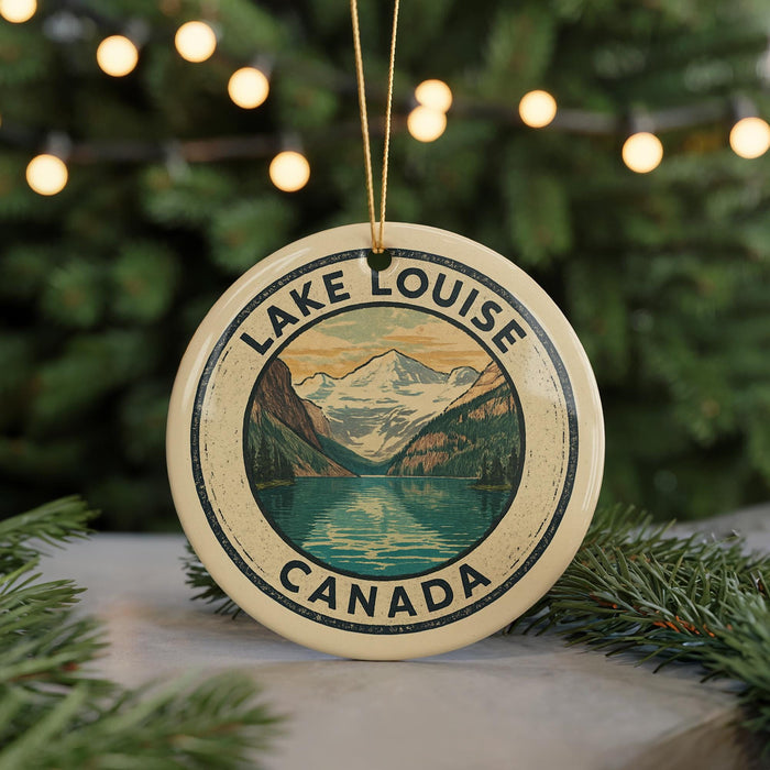 A circular ornament with a mountain landscape and a lake, surrounded by greenery, is displayed in front of a blurred background with Christmas lights.