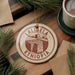 A circular ornament with the text "LALIBELA ETHIOPIA" printed on it, surrounded by pine branches and a cup of coffee on a wooden surface.