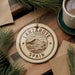 A circular ornament with the text "LANZAROTE SPAIN" printed on it, surrounded by pine branches and a cup of coffee on a wooden surface.