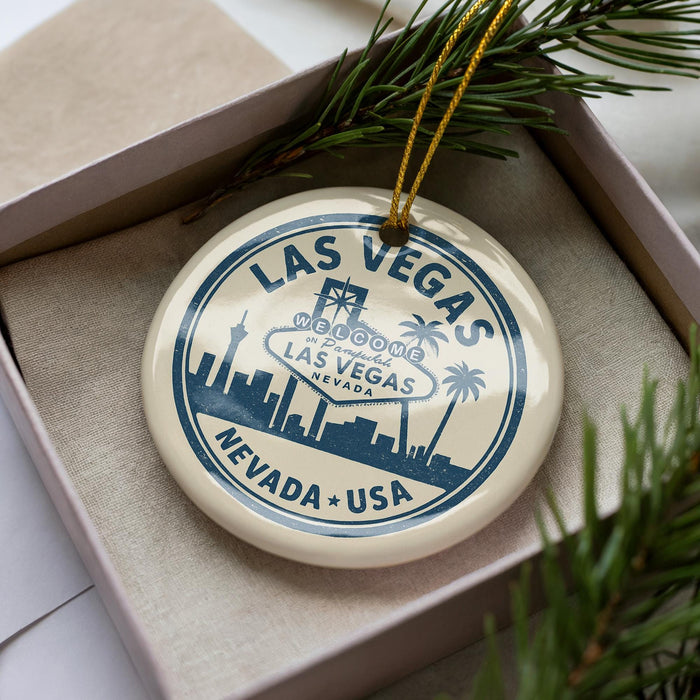 A circular ornament with the text "LAS VEGAS" and "WELCOME LAS VEGAS NEVADA, USA" printed on it, placed in a box with pine branches.