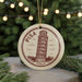 A circular ornament featuring the Leaning Tower of Pisa, a famous landmark in Italy, surrounded by Christmas lights and greenery.