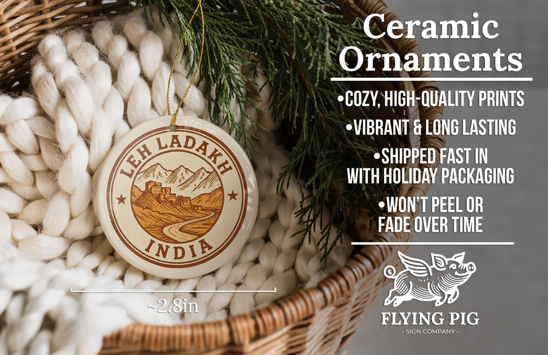 Ceramic ornaments, specifically a round ornament with a mountain and castle design, hanging in a basket with pine branches.