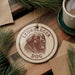 A circular ornament featuring a dog's head and the text "LEONBERGER DOG" is displayed on a wooden surface, surrounded by pine branches and a cup of coffee.