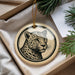 A round ornament featuring a leopard's face is displayed in a box, surrounded by pine branches.