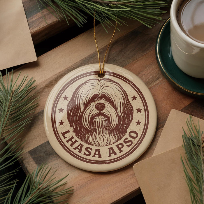 A circular ornament featuring a dog's face and the text "LHASA APSO" is displayed on a wooden surface, surrounded by pine branches and a cup of coffee.