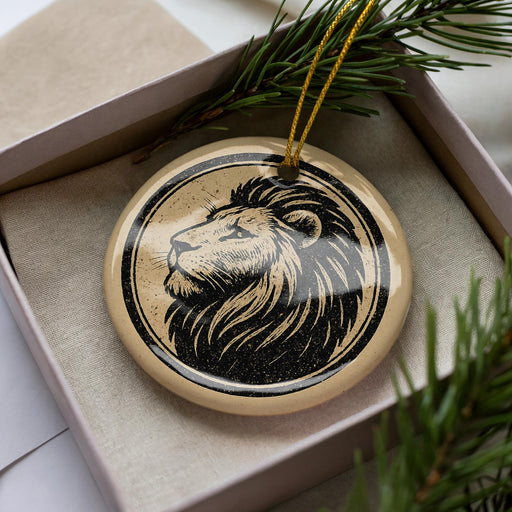 A circular ornament with a lion's head design is displayed in a box, surrounded by pine branches.