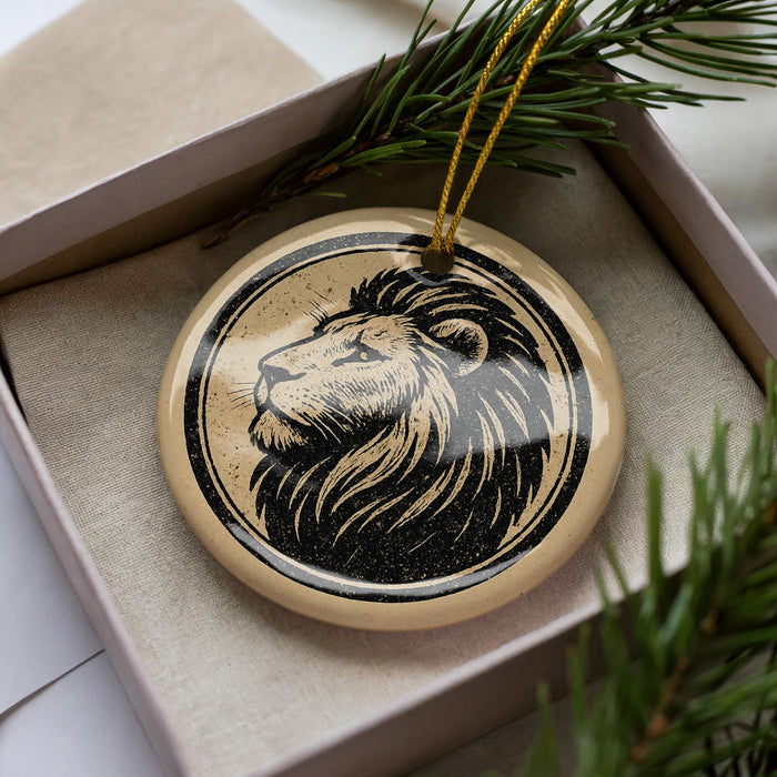 A circular ornament with a lion's head design is displayed in a box, surrounded by pine branches.