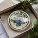 A circular ornament with a lionfish design, placed in a box with pine branches.