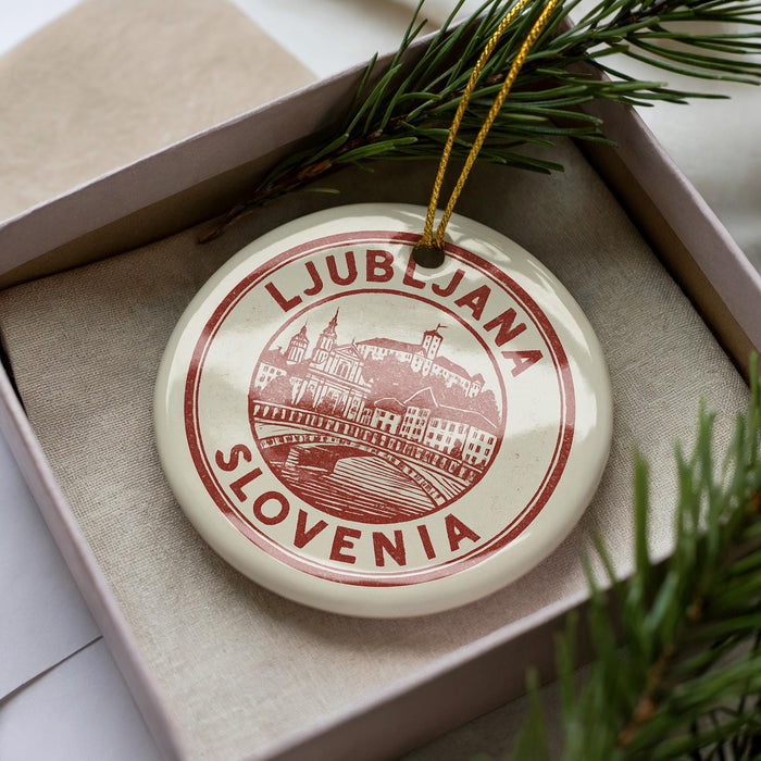 A circular ornament with the text "LJUBBLJANA SLOVENIA" printed on it, placed inside a box with pine branches.