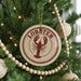 A Christmas tree decorated with a round ornament featuring a lobster design, surrounded by beaded ornaments and twinkling lights.