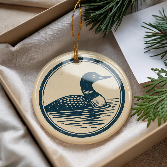 A decorative ornament featuring a loon, a type of bird, is displayed in a box with pine branches.
