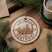 A circular ornament with the text "LOUISVILLE KENTUCKY USA" printed on it, surrounded by pine branches and a cup of coffee on a wooden surface.
