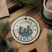 A circular ornament with the text "LUSAKA ZAMBIA" and a graphic of a city skyline, hanging on a wooden surface.