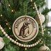 A round ornament on a Christmas tree featuring a penguin design, with the text "MAGELLANIC PENGUIN" around the edge.
