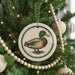 A ceramic ornament featuring a duck is hanging on a Christmas tree, surrounded by lights and ornaments.