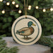 A ceramic ornament featuring a duck is displayed on a table, with a blurred background of a Christmas tree and twinkling lights.