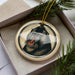 A decorative ornament featuring a close-up image of a monkey's face, with a beige background and a black border.