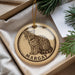 A round ornament with a cat illustration and the name "MARGAY" printed on it, placed in a box with pine branches.