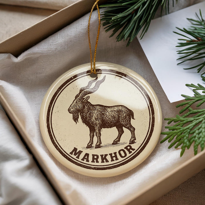 A circular ornament with a brown and white design featuring a goat, and the word "MARKHOR" written below it.