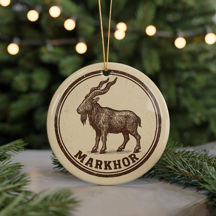 A circular ornament featuring a brown goat with curved horns, surrounded by a decorative border, is displayed in front of a blurred Christmas tree.