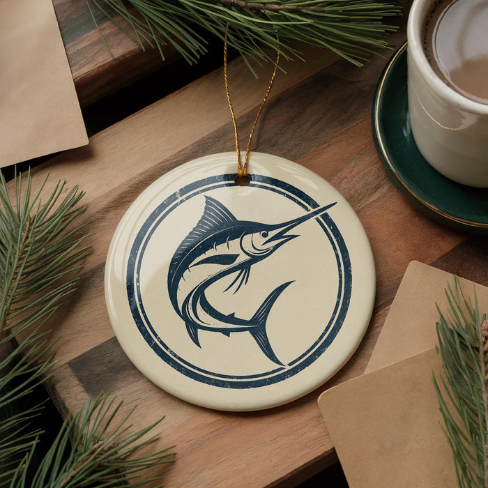 a round ceramic ornament with a blue and white design depicting a fish, placed on a wooden surface alongside a cup of coffee and some pine branches.