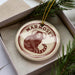 A round ornament with a marmoset monkey image, placed in a box with pine branches.