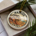 A circular ornament with the text "MASADA ISRAEL" printed on it, surrounded by a border and a mountain illustration.