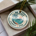 A circular ornament with the text "MAUI HAWAII USA" printed on it, surrounded by a palm tree and a sunset.