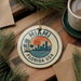 A circular ornament with the text "MIAMI FLORIDA USA" and a graphic of a city skyline with palm trees, hanging on a wooden surface.