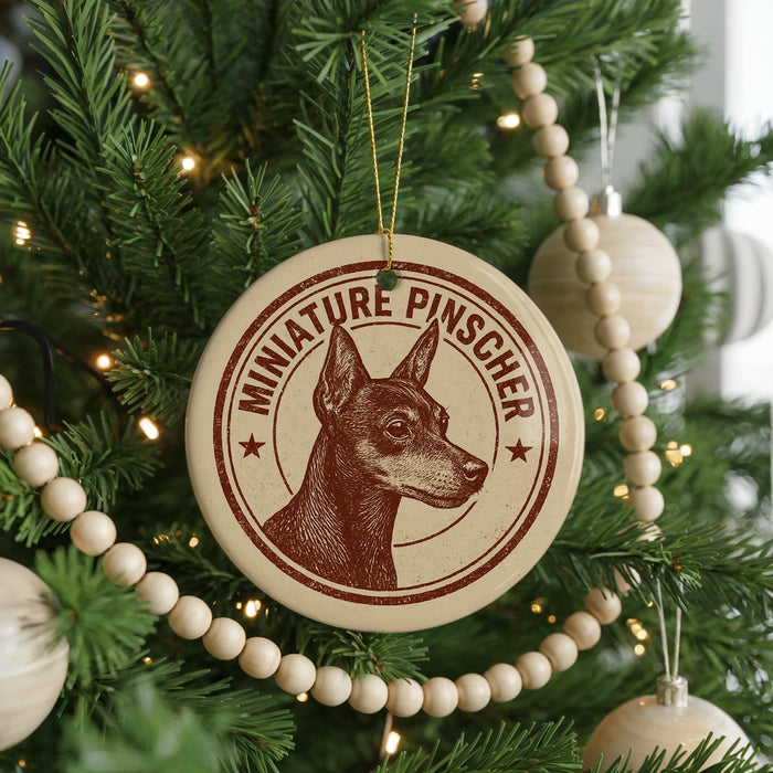A Christmas tree decorated with ornaments, including a circular ornament with a dog's head and the text "MINIATURE PINSCHER" printed on it.