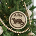 A Christmas tree decorated with ornaments, including a circular ornament with a picture of a brown animal and the word "MINK" written on it.