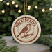 A round ornament with the text "MOCKINGBIRD" and an illustration of a bird perched on a branch, hanging from a string.