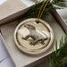 A ceramic ornament in the shape of a lizard, with a brown and beige color scheme, is displayed in a box with pine branches.