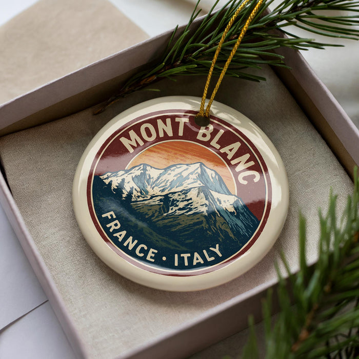 A decorative ornament in a box, featuring a mountain landscape with the text "MONT BLANC FRANCE ITALY" around the edge.